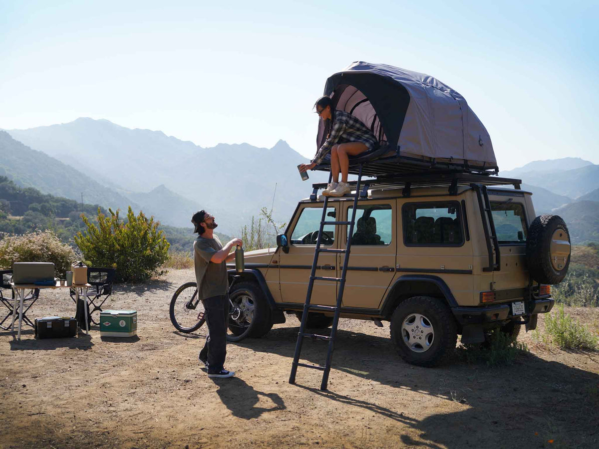C6 Rev Rooftop Tent X (HellaStorm) – on a vehicle roof at camp, person at the ladder