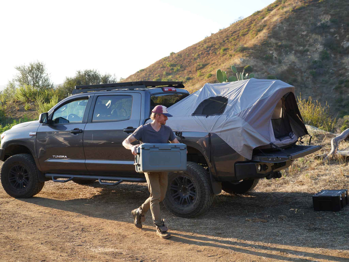 C6 Rev Pickup Truck Tent – person carrying a cooler beside a truck with the tent set up
