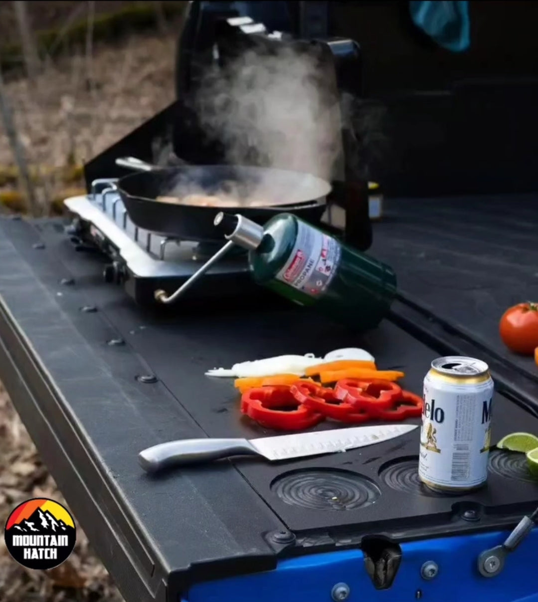 Cooking on a Mountain Hatch Tacoma tailgate table with a single-burner stove, peppers and a drink in the holder