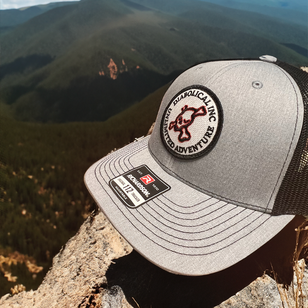 Gray Diabolical Inc trucker hat on a rock above a mountain valley