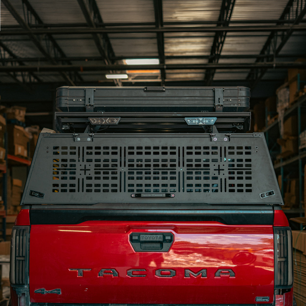 Rear hatch closed on a bed rack at the back of a red truck with a roof-mounted case above