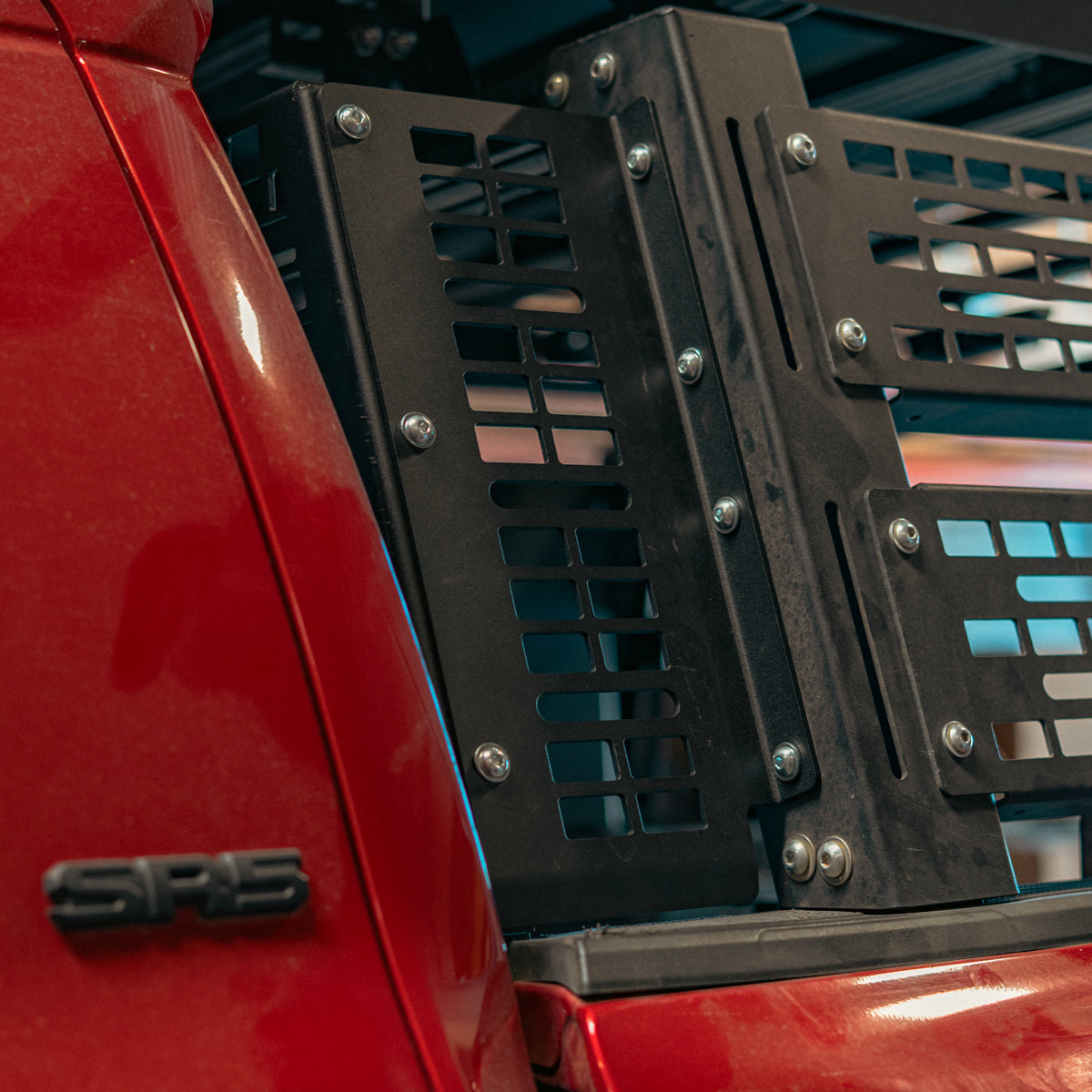 Bolted corner of a black MOLLE side panel beside a red truck cab