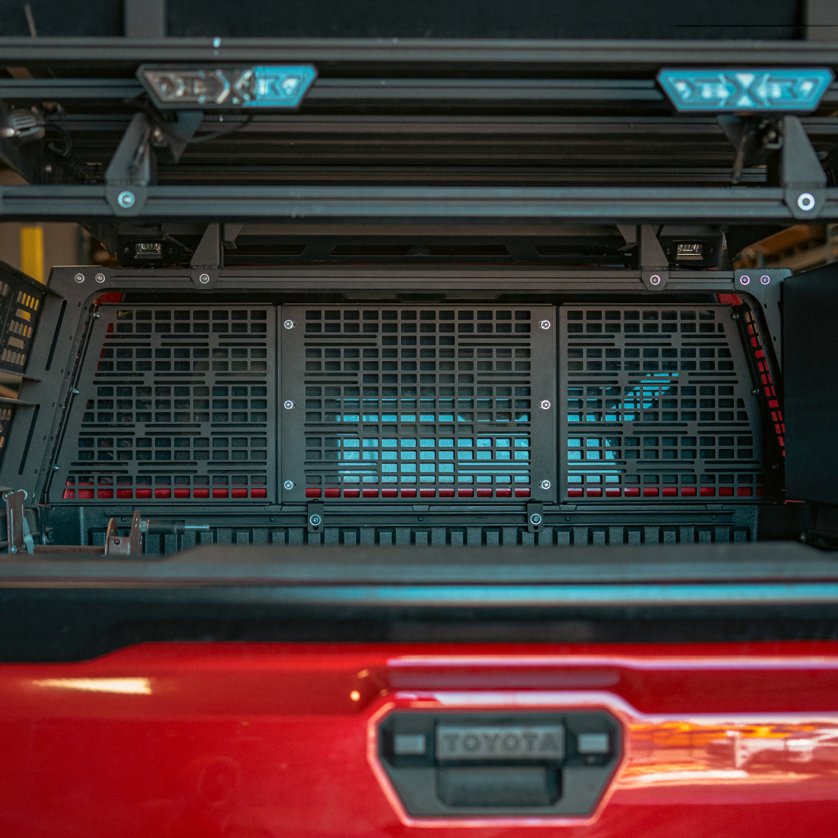 Rear view of a three-panel MOLLE headache rack inside a bed rack on a red truck