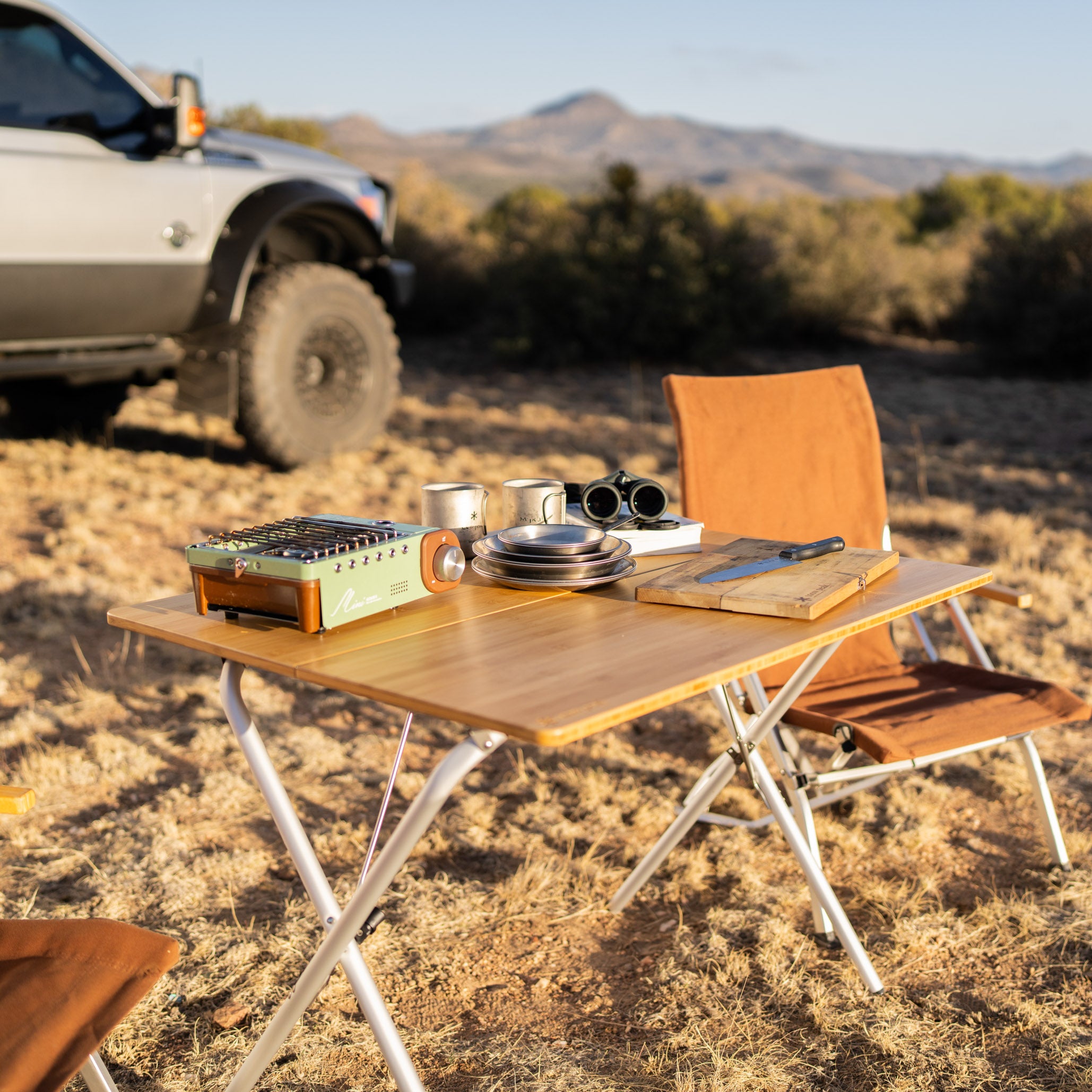 Snow Peak Single Action Table Medium in campsite with plates and cutting board and stove