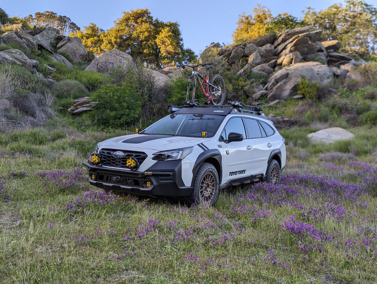 White Subaru wagon on a grassy hillside with a roof rack