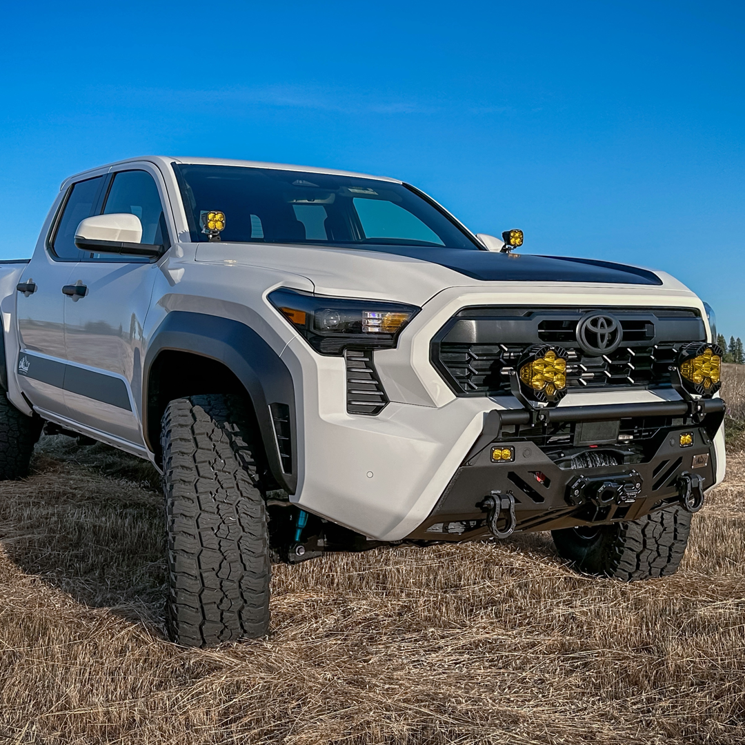 White Toyota truck with amber light pods and a front bumper parked on dry grass