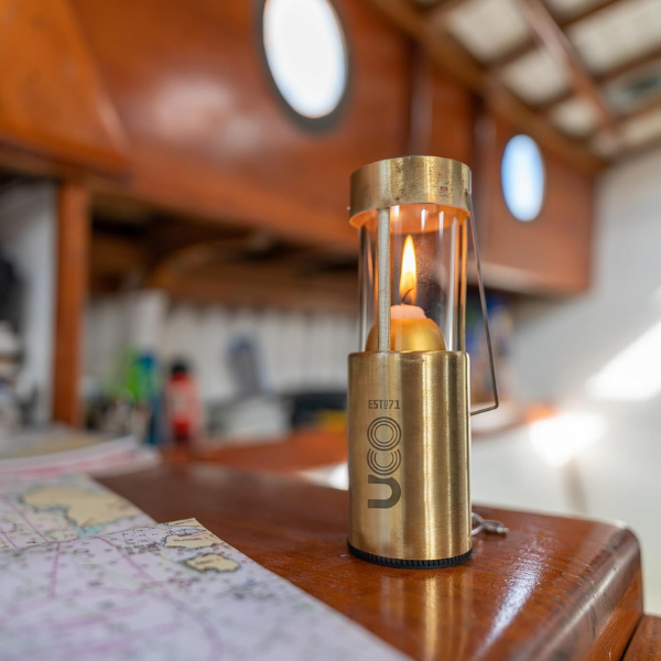 Brass UCO Candlelier candle lantern hanging outdoors near a campfire while a person in gloves tends the fire