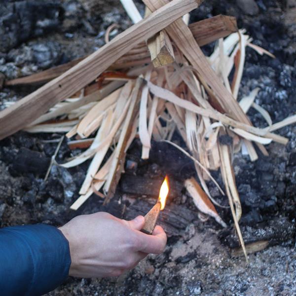 Hand striking a UCO fire starter, with sparks catching kindling to start a fire