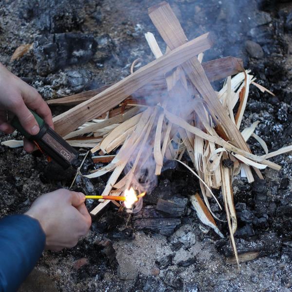 Hand striking a UCO Titan stormproof match to light kindling in a campfire