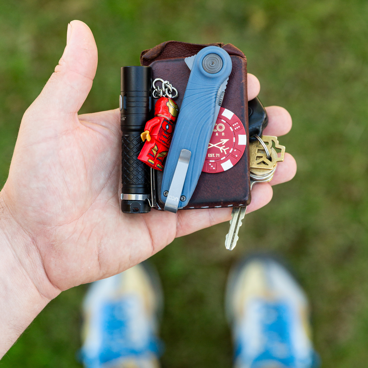 Hand holding a wallet-style EDC organizer with a blue UCO Whidbey Mini folding knife tucked inside