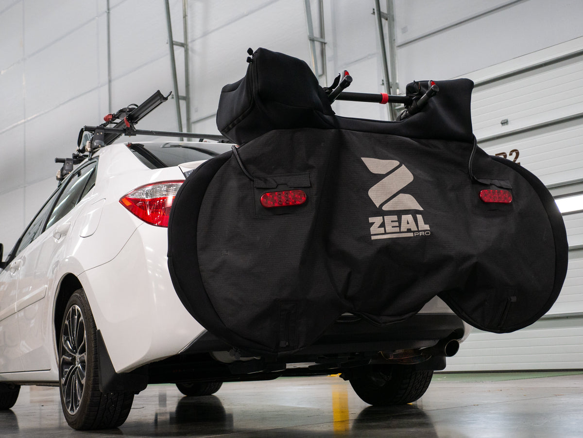 Covered road bike on a hanging hitch rack with a top tube adapter behind a white sedan