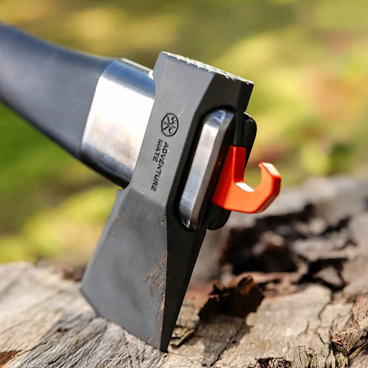 Close-up of the Adventure Mate axe head embedded in a log, showing the logo and orange hook