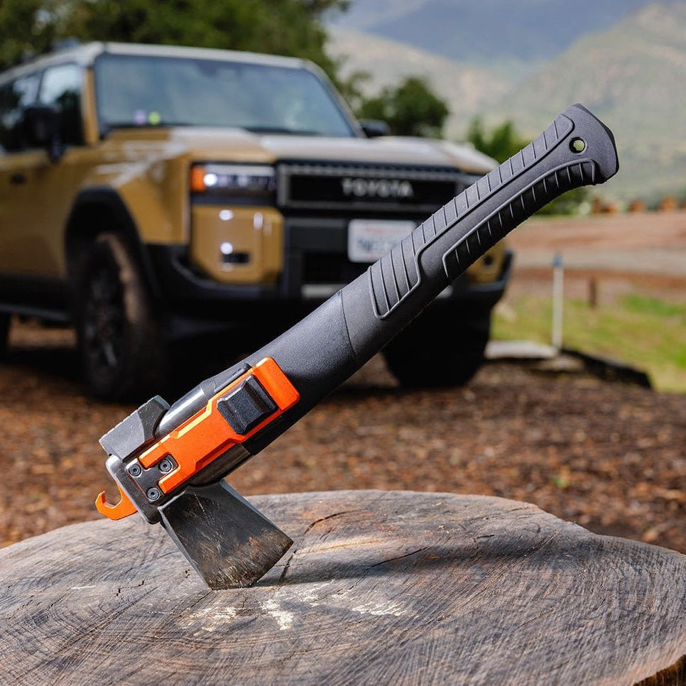 Adventure Mate axe embedded in a tree stump with the handle angled up, and a tan SUV in the background