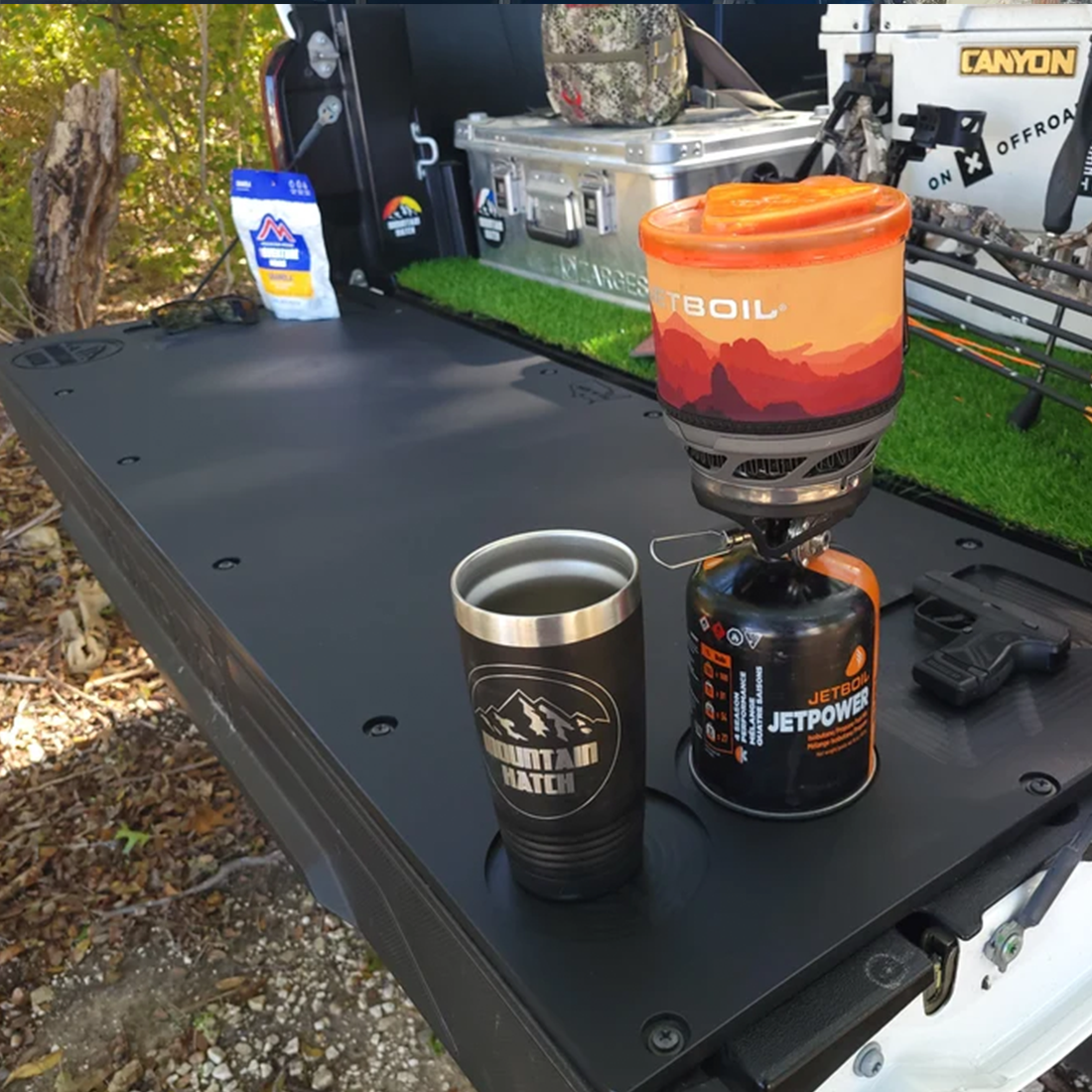 Mountain Hatch tailgate table on a GM truck tailgate with a Jetboil stove and insulated mug in the drink holder (representative photo for the 2022+ Silverado/Sierra HD panel)