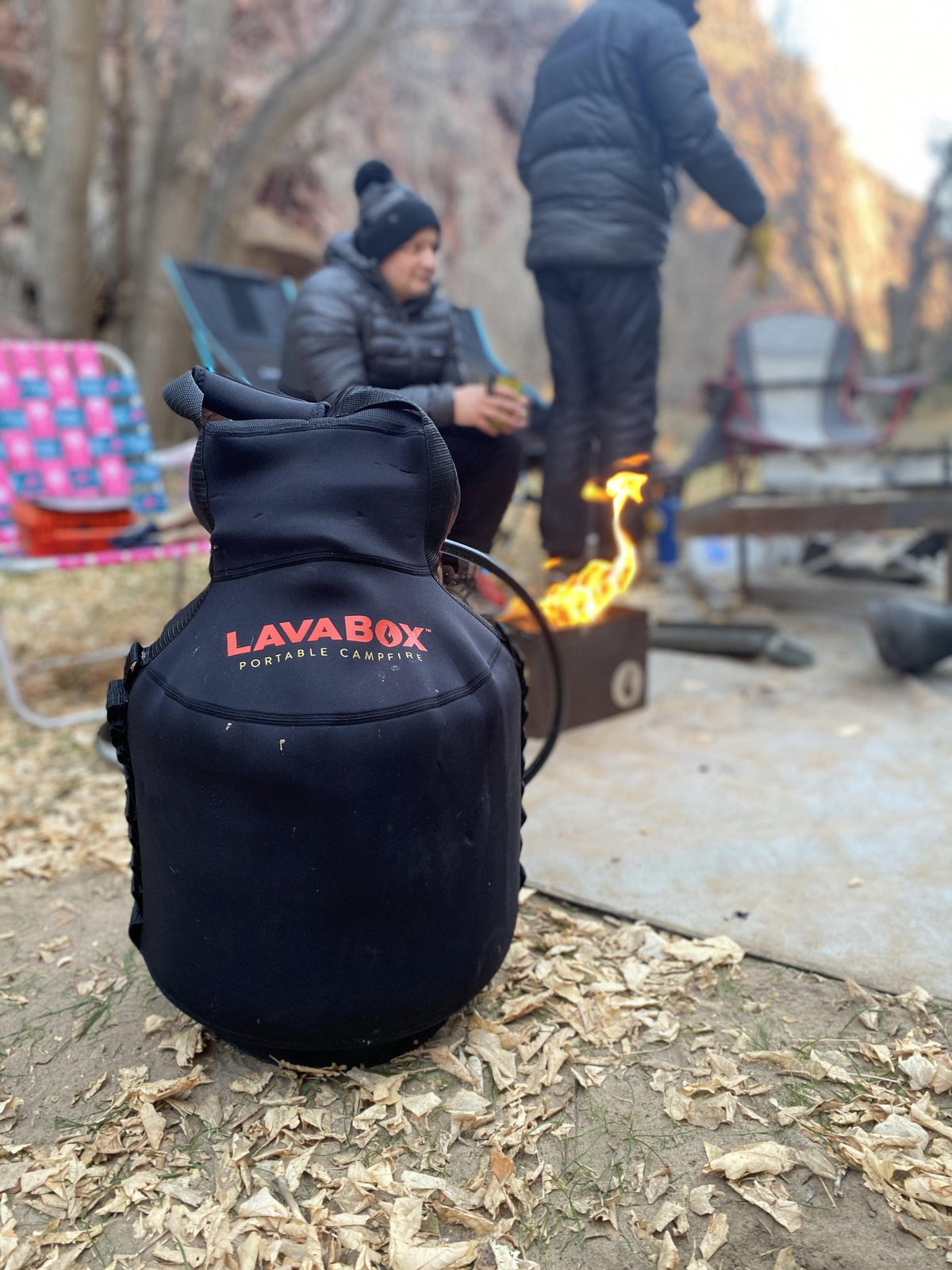 Lifestyle photo of two people at a campsite with a navy LAVABOX tank top propane tank cover in the foreground and a lit fire pit behind them