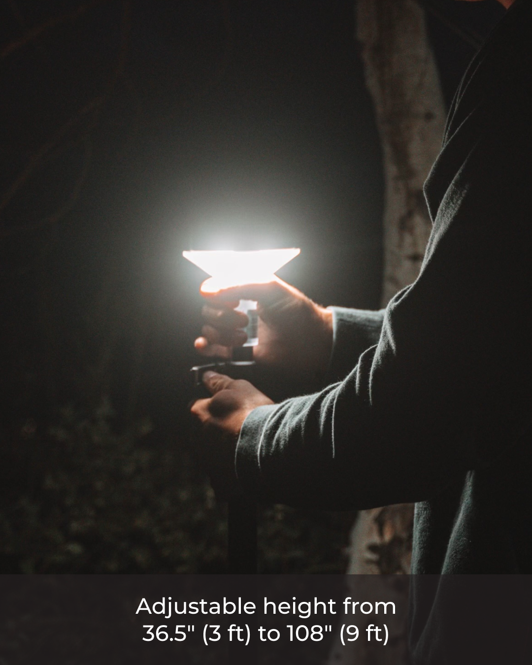 Person holding a portable light source with adjustable height feature in a dark setting.