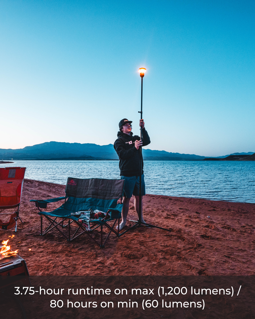 Person holding a camping lantern on a beach with mountains in the background