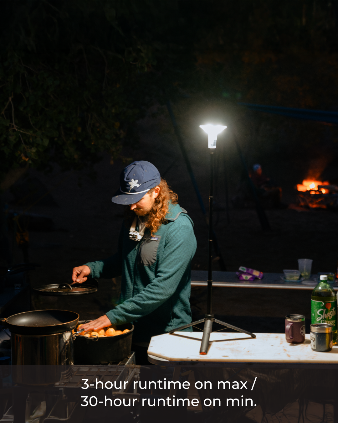 Person cooking outdoors at night with a portable Devos Mini Light illuminating the area.