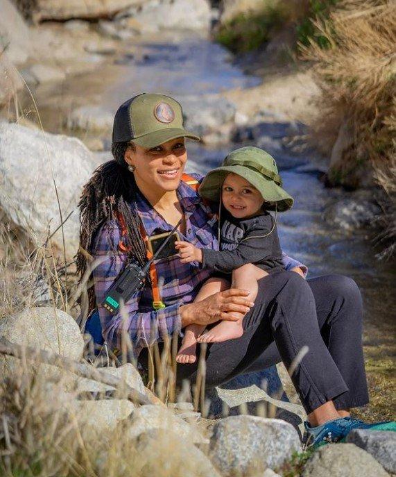 Lifestyle photo of a woman and child sitting together on rocks near a stream, both wearing olive LAVABOX caps