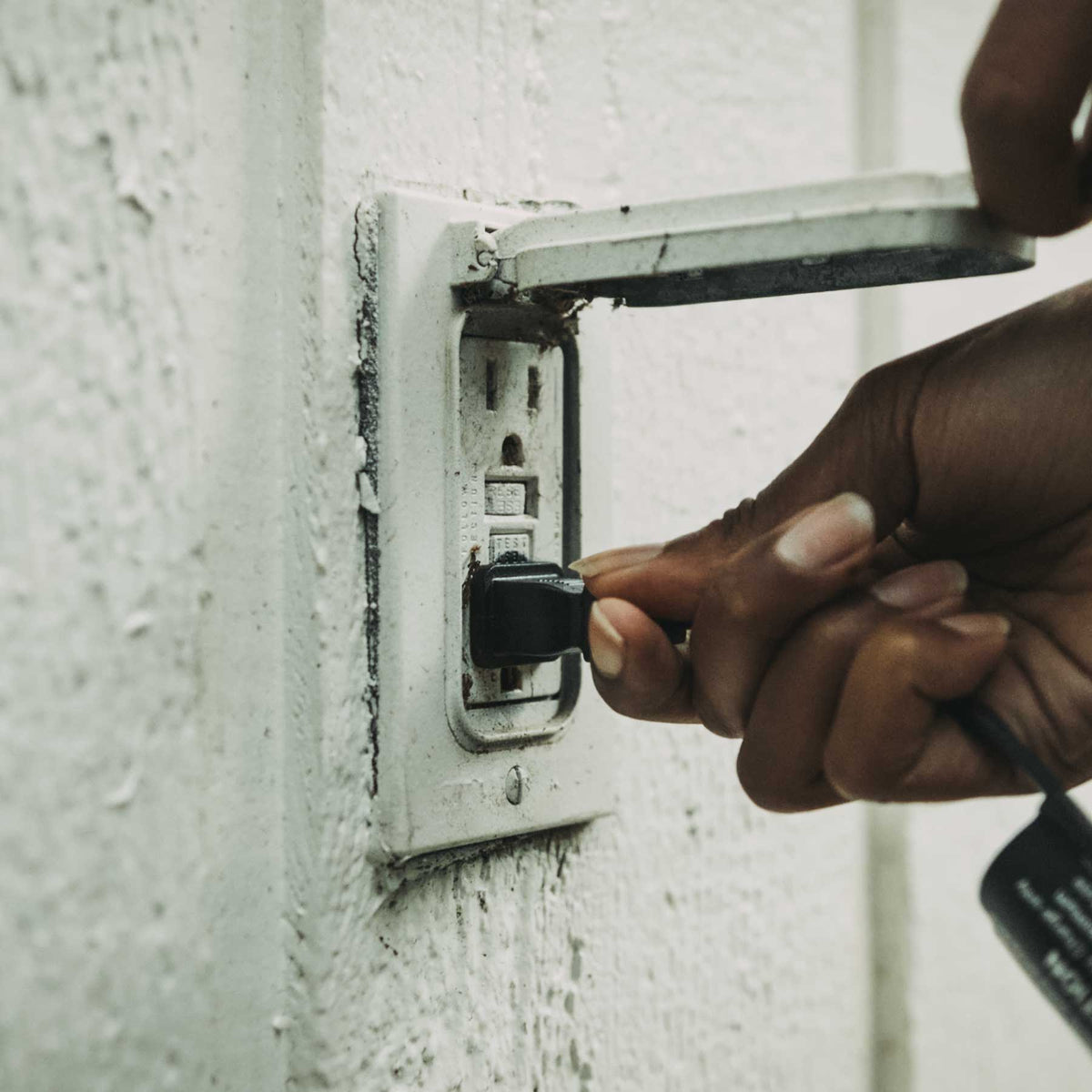 Hand plugging a cord into a wall outlet