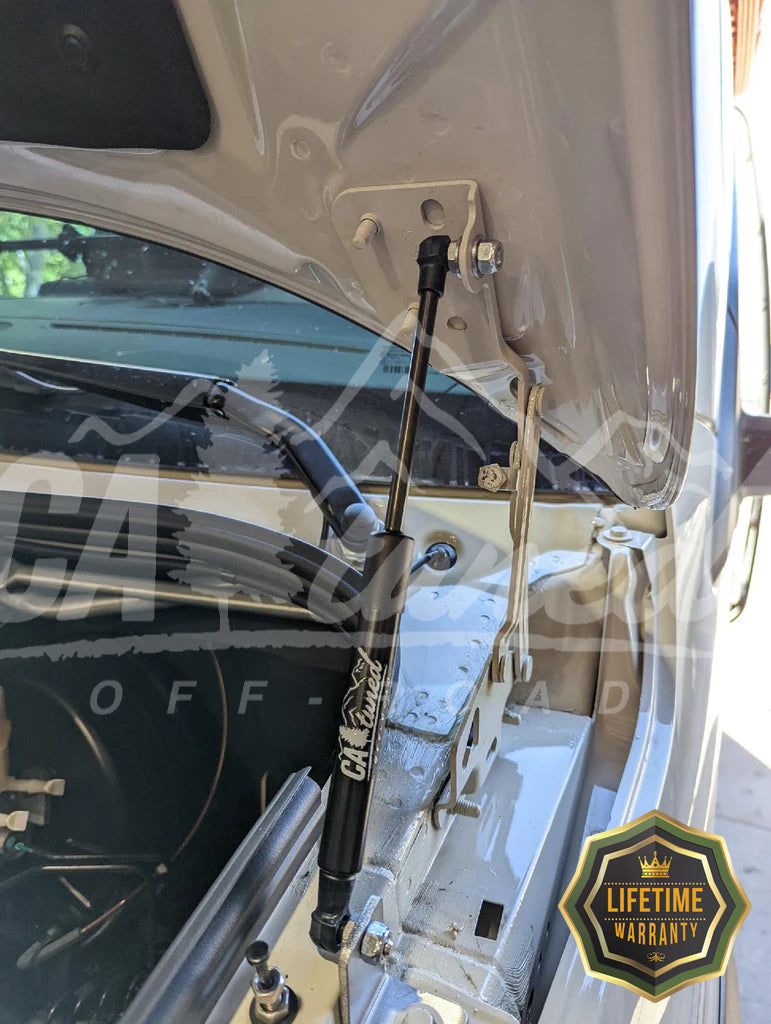 Hood strut holding a van hood open, with a lifetime warranty badge in the corner