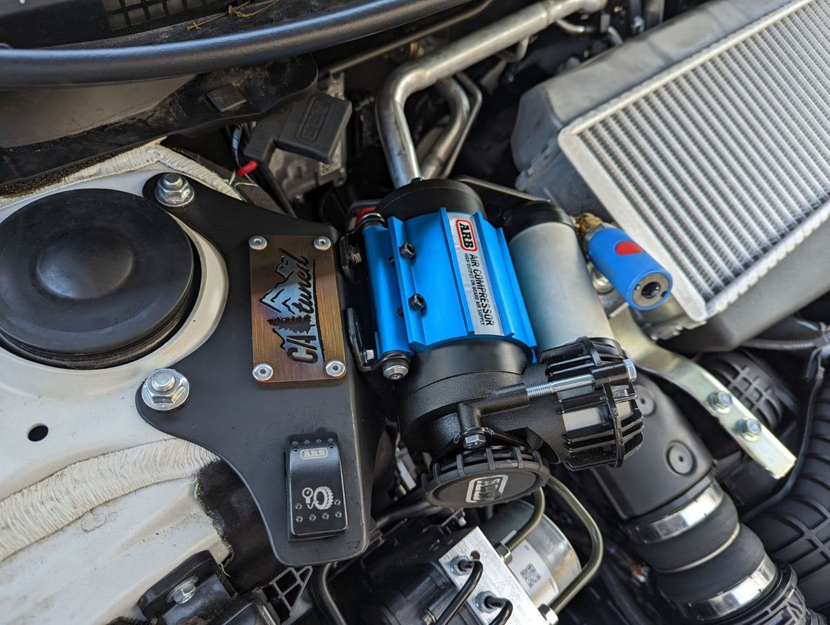 Compressor on a black bracket with a switch visible in an engine bay
