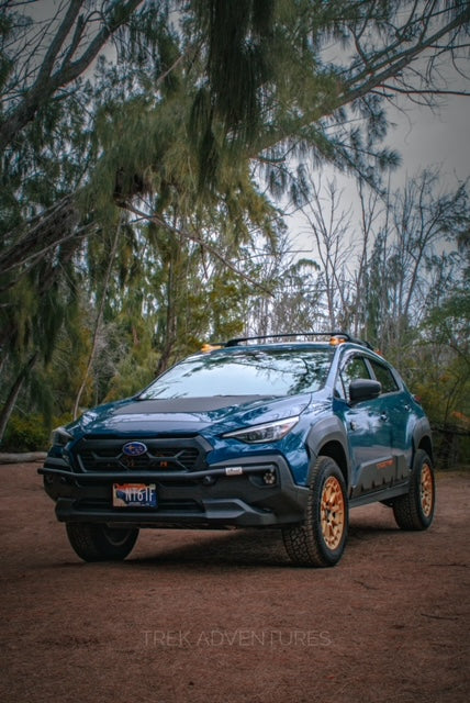 Front three-quarter view of a blue Subaru SUV with a black brush bar on a dirt lot