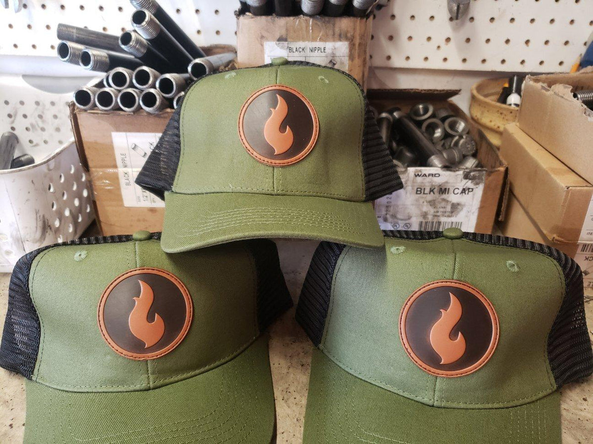 Three olive green trucker-style caps with a flame logo patch, stacked on a shop shelf