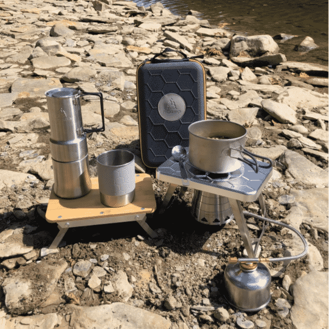 Camping stove and cookware set up on a rocky surface near water