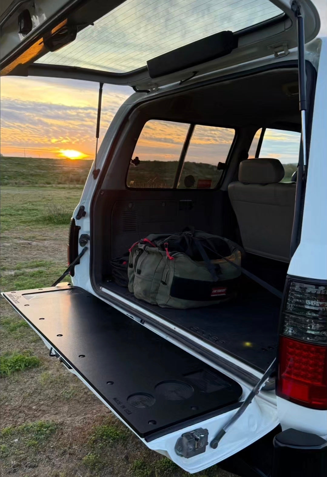 80 Series Land Cruiser at sunset with the rear hatch open and the Mountain Hatch panel on the lowered tailgate