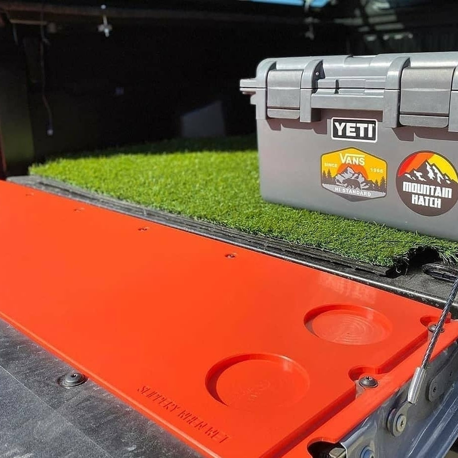 Orange Mountain Hatch tailgate table with YETI cooler and turf mat showing the recessed drink holders (color shown is not the standard Black)