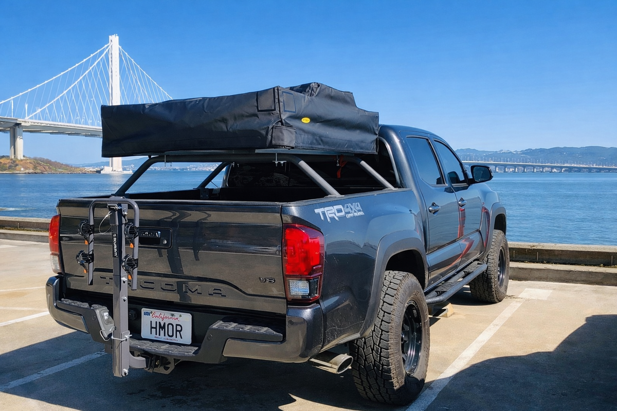 Gray Tacoma with HMOR bed bars, rooftop tent and hitch bike rack by the water