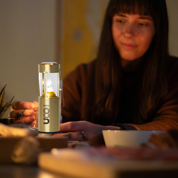 Brass UCO Candlelier candle lantern sitting unlit on a wood table indoors